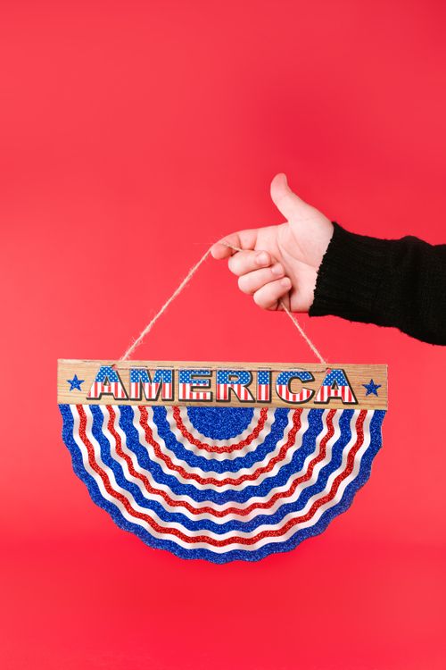 Free A hand holding a colorful American patriotic decoration against a red backdrop. Stock Photo
