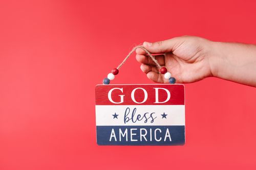 Free Patriotic sign with 'God Bless America' held by hand against a red background. Stock Photo