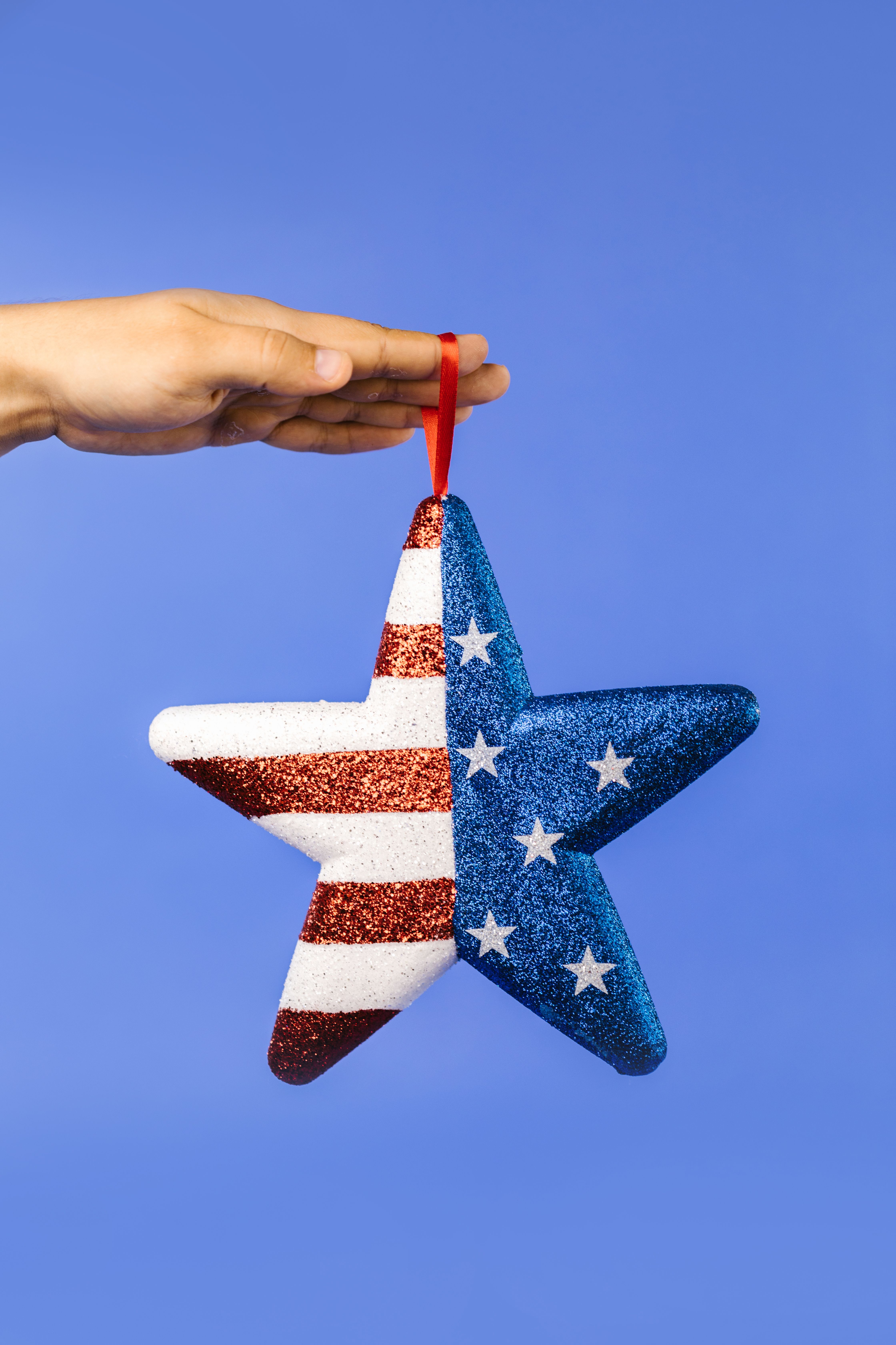 Glittery star ornament with US flag design held by a hand against a blue backdrop.