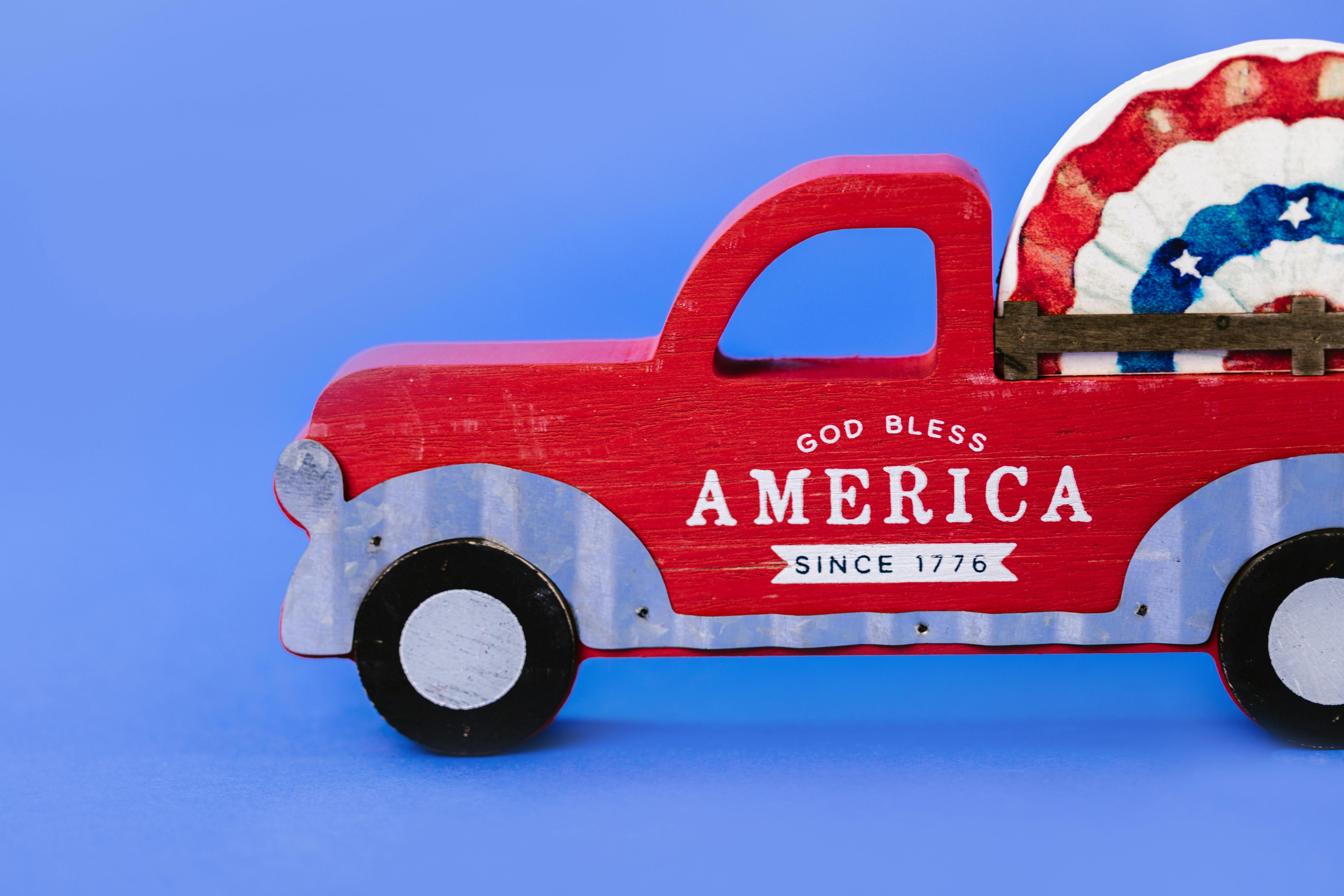 Red wooden toy truck with God Bless America text on blue background.