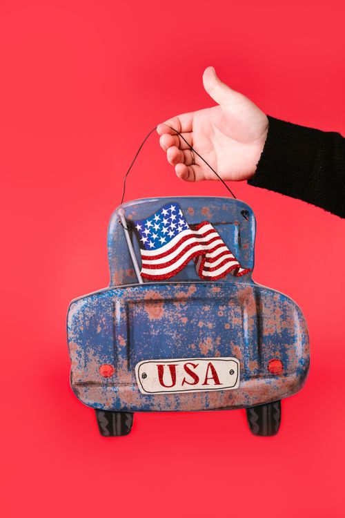 Free Rustic blue car ornament held by hand with USA flag, ideal for patriotic themes. Stock Photo