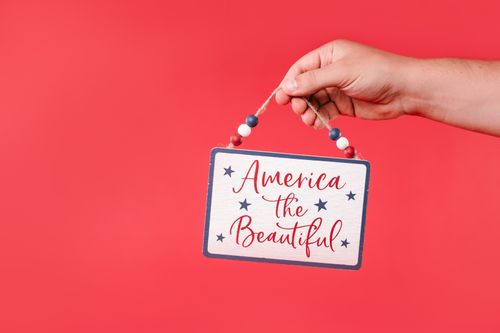 Free A hand holds a decorative patriotic sign on a vibrant red background. Stock Photo