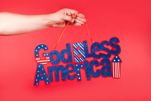 Free A close-up of a hand holding a 'God Bless America' sign on a red background, perfect for Independence Day themes. Stock Photo