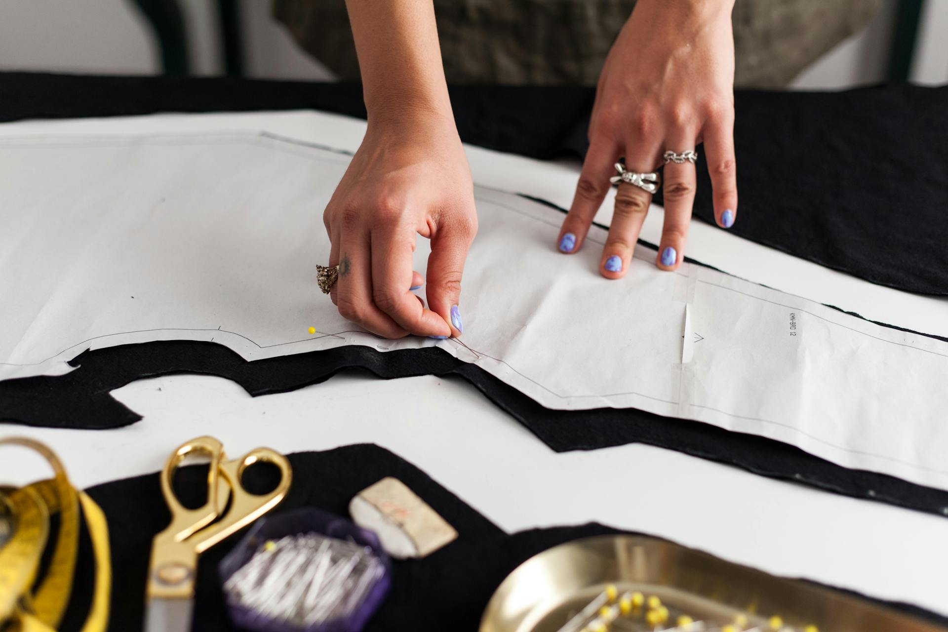 Close-up of hands pinning a sewing pattern onto black fabric, showcasing design process.