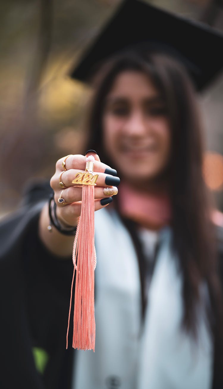 Woman In Graduation Gown Holding A Pin With Graduation Year 