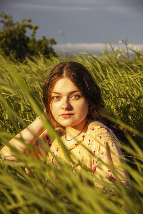 Free Portrait of a young woman sitting in a sunlit green grass field, captured outdoors. Stock Photo