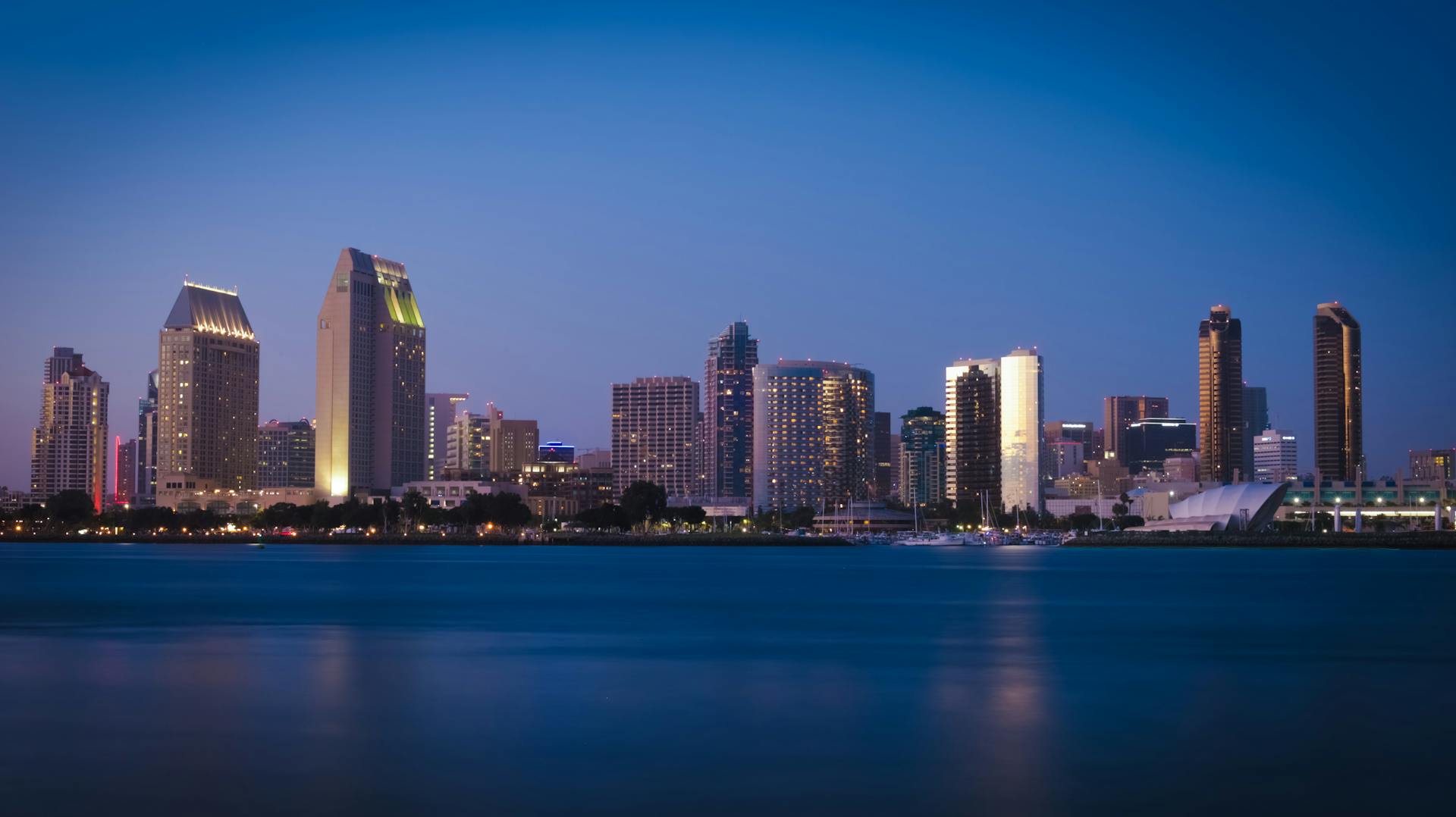 Illuminated San Diego skyline reflecting on water at dusk, showcasing modern architecture.