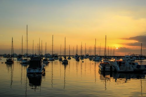 Free A serene view of sailboats docked at Manila Harbor during a stunning sunset, reflecting on the water. Stock Photo