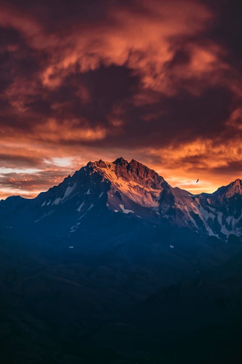 Free Breathtaking view of mountain range covered with snow under cloudy colorful sky at sundown Stock Photo