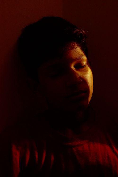 Free A dramatic close-up portrait of a man in a red shirt under warm moody lighting. Stock Photo