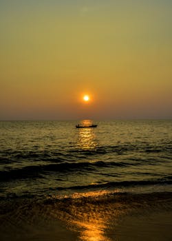 A tranquil fishing boat silhouetted against a stunning golden sunset over the Indian Ocean.