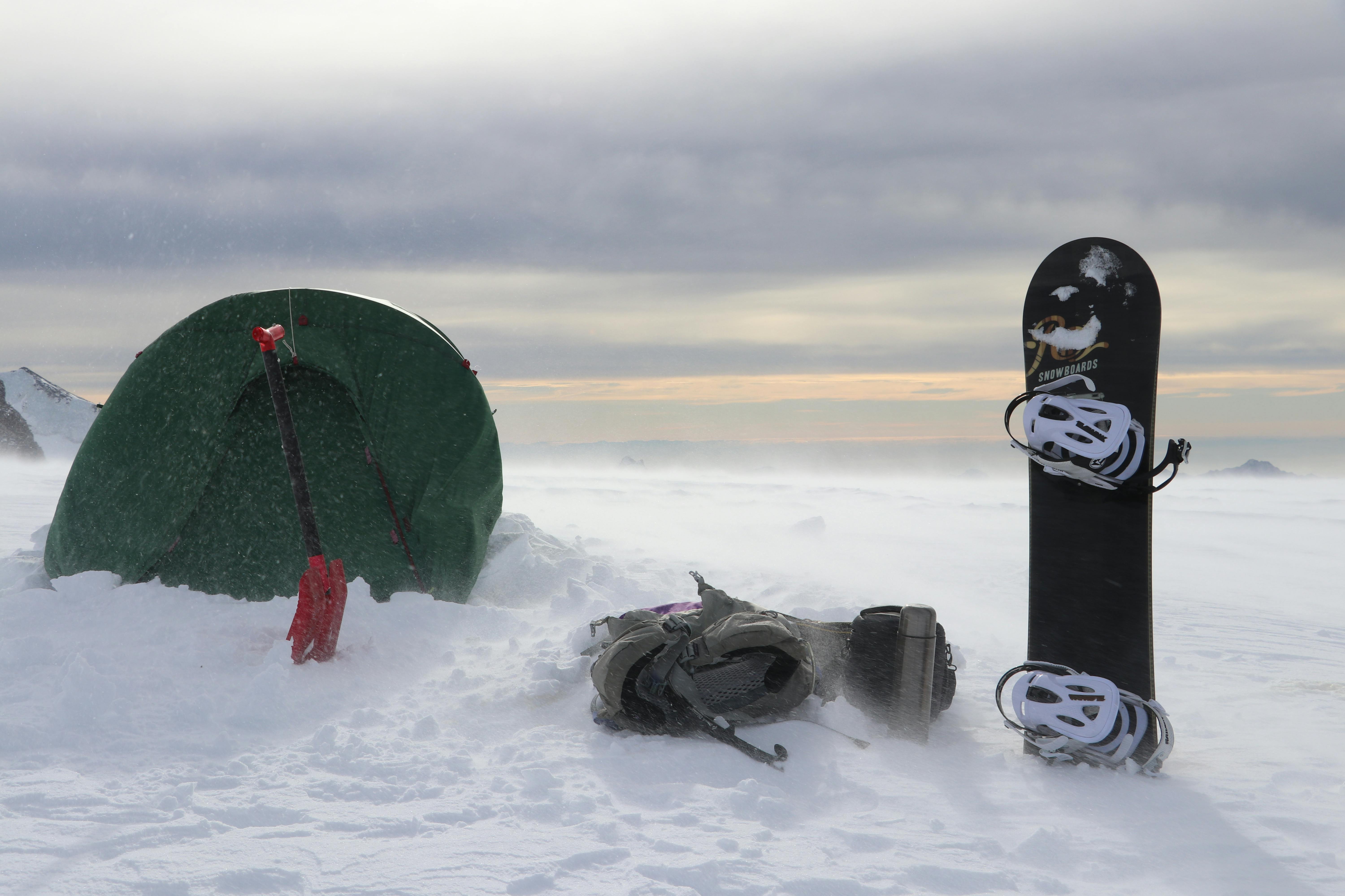 Prescription Goggle Inserts - Snowy mountain camping setup with a tent, snowboard, and backpack in winter.