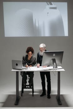 Two professionals collaborate in a high-tech setting with laptops and digital screens.