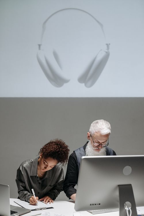 Free Two professionals collaborating on product design with a computer and notes in a creative lab. Stock Photo