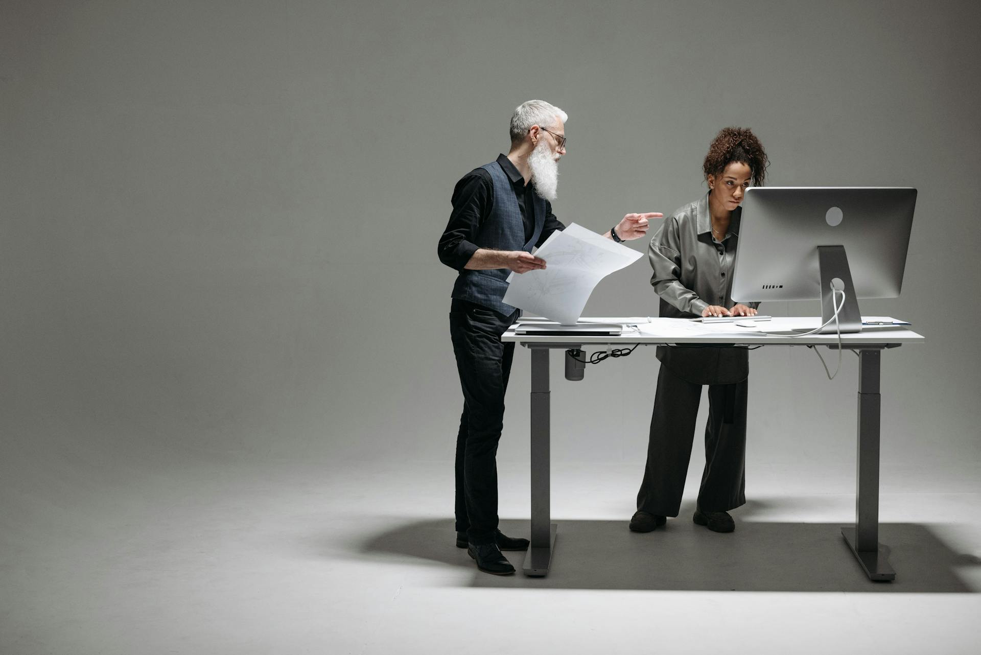 A senior man and a woman working together at a desk in a modern office setting, focusing on a project.