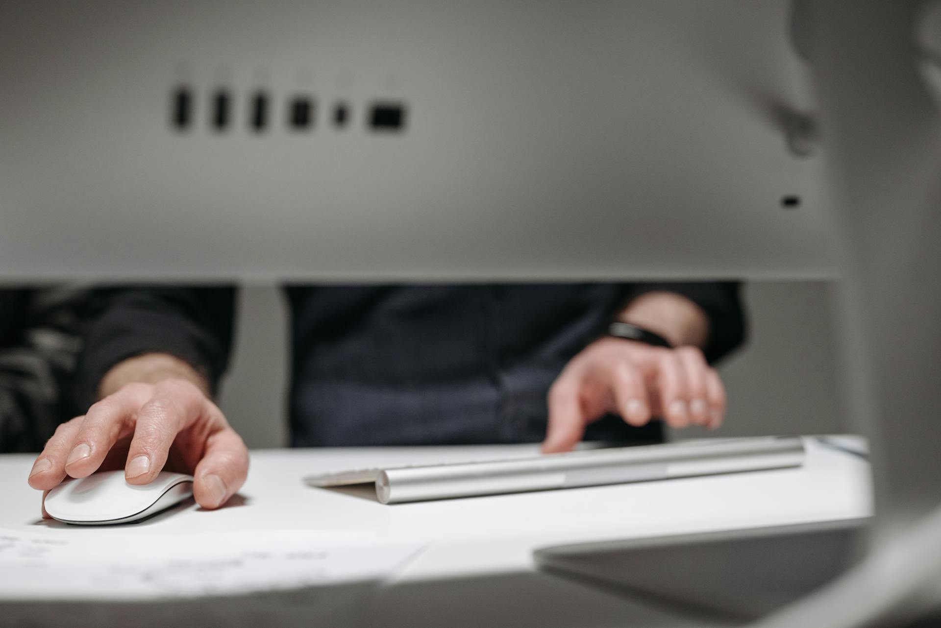 A focused close-up of hands typing on a sleek, modern computer setup in an office environment.