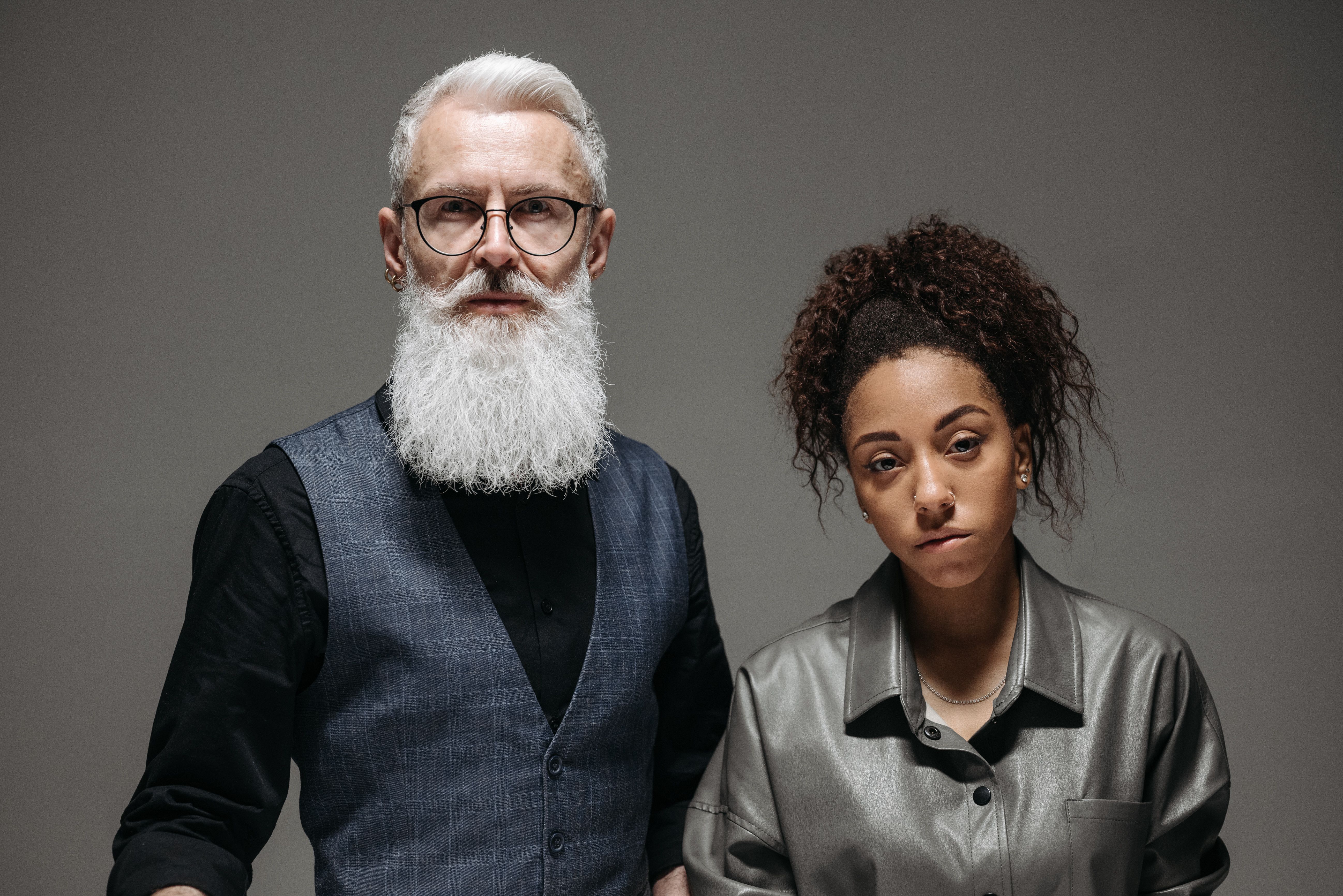Portrait of a diverse duo with elderly man and young woman in stylish attire against a gray background.