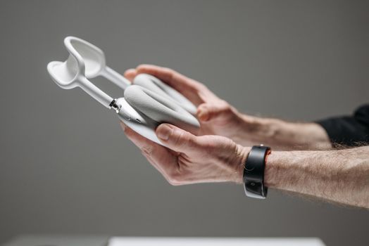 Close-up of hands holding white wireless over-ear headphones against a grey background.