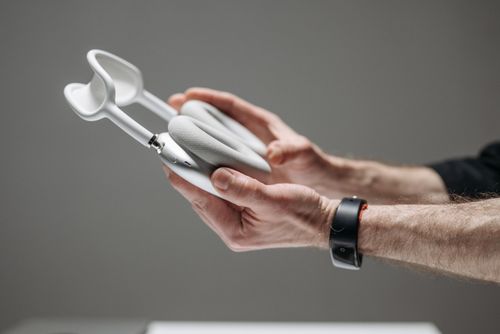 Free Close-up of hands holding white wireless over-ear headphones against a grey background. Stock Photo