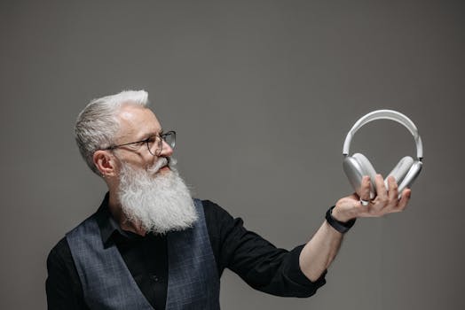 Bearded senior man in corporate attire holds stylish wireless headphones in studio setting.