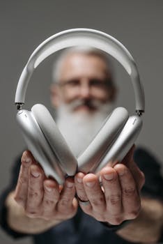 An adult holds sleek silver wireless headphones, focusing on modern audio technology.