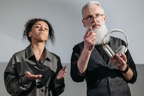 A Woman Doing Hand Gestures with a Man Holding Wireless Headphones