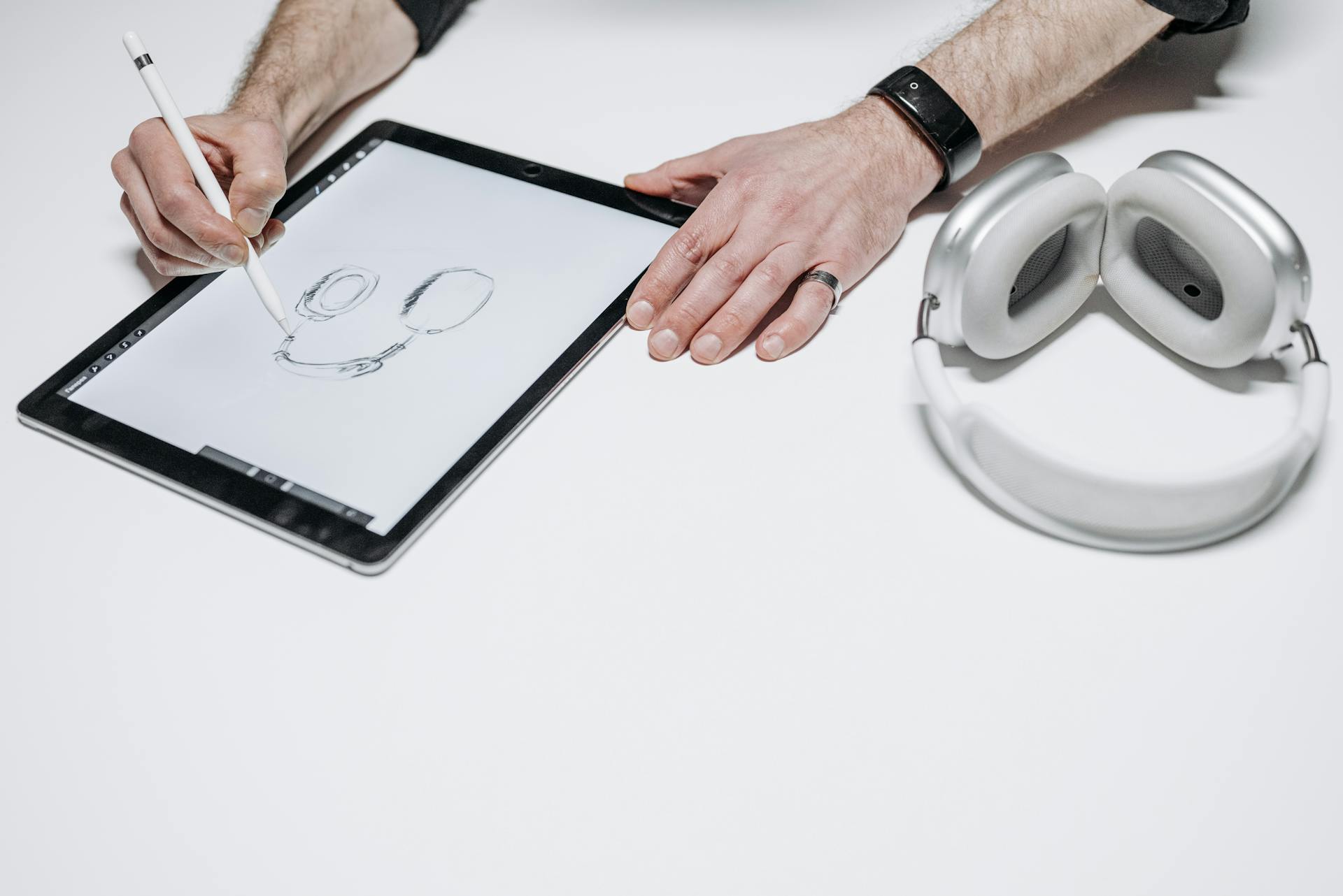 A person sketching headphones on a tablet with a stylus, showcasing digital design creativity.