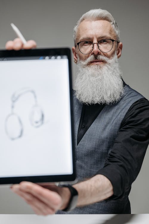 A Bearded Man in Black Long Sleeves Wearing Eyeglasses while Holding a Tablet