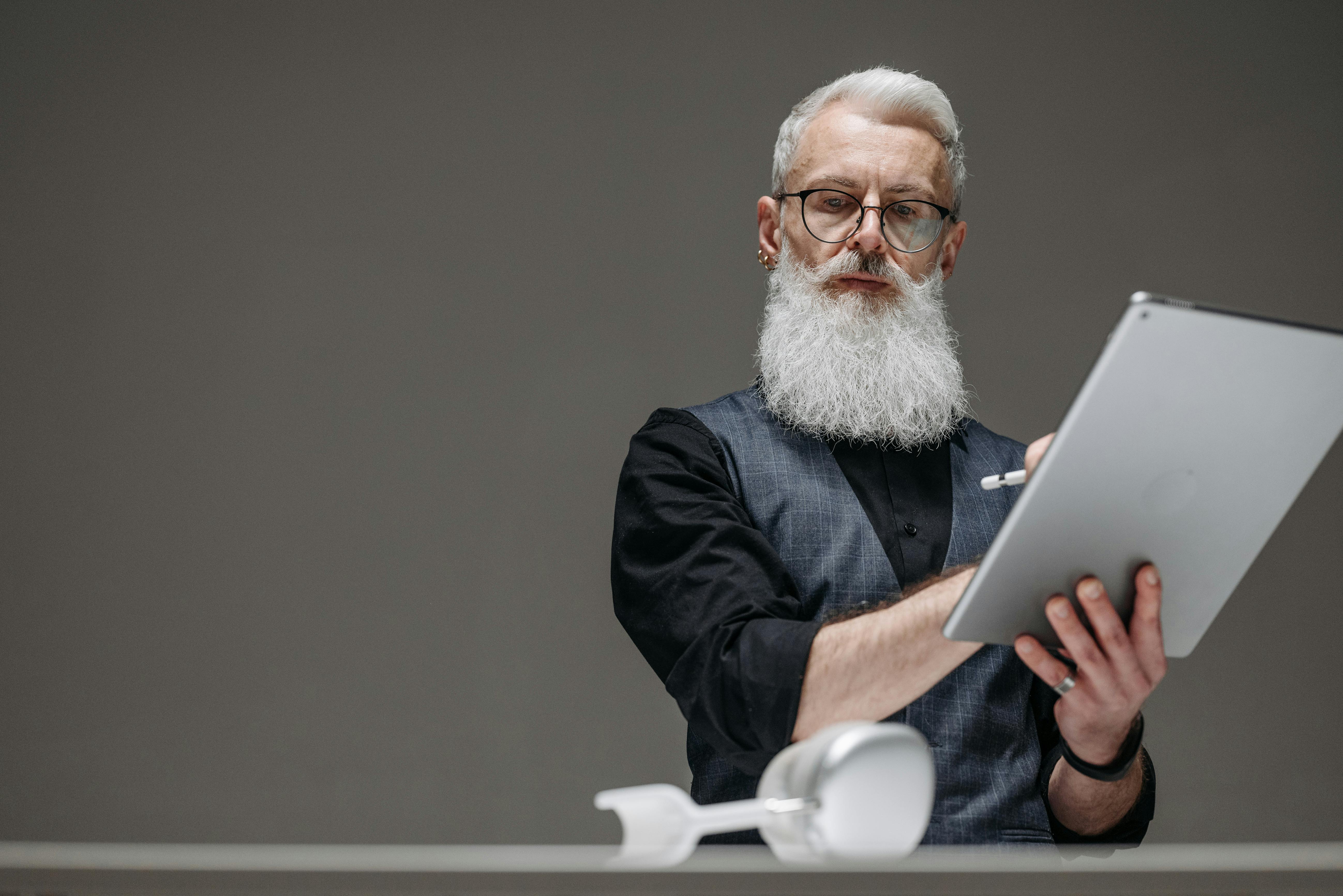 an elderly man looking at the headphones while holding a tablet