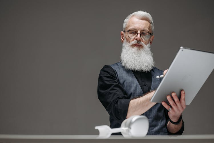 An Elderly Man Looking At The Headphones While Holding A Tablet