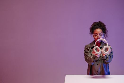 An African American woman holding headphones against a vibrant pink background in a studio setting.