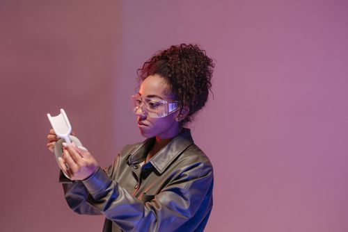 Free A woman in a leather jacket examines protective goggles against a pink background. Stock Photo