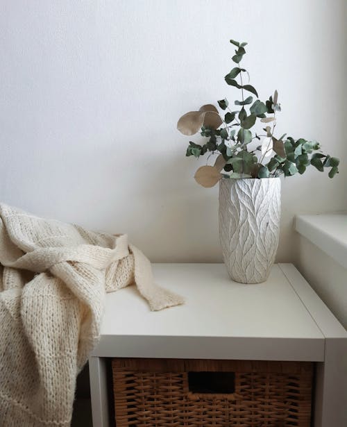 White Ceramic Vase with Dried Leaves on White Wooden Table