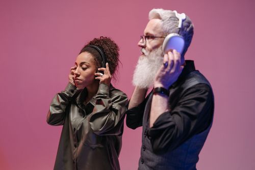 Free Man and woman listening to music on headphones against a pink background. Stock Photo