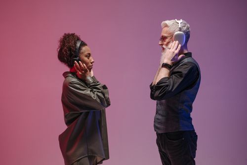 Free An adult man and woman facing each other in a studio, wearing wireless headphones against a purple backdrop. Stock Photo