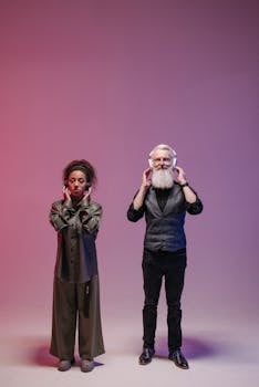 An elderly bearded man and a woman enjoying music with headphones in a studio setting.