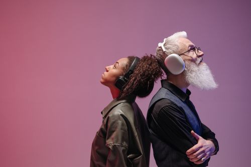 Free A black woman and a caucasian man with headphones enjoying music back to back in a colorful studio setup. Stock Photo