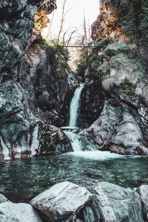 Free A tranquil waterfall cascading through a rocky gorge surrounded by lush greenery. Stock Photo