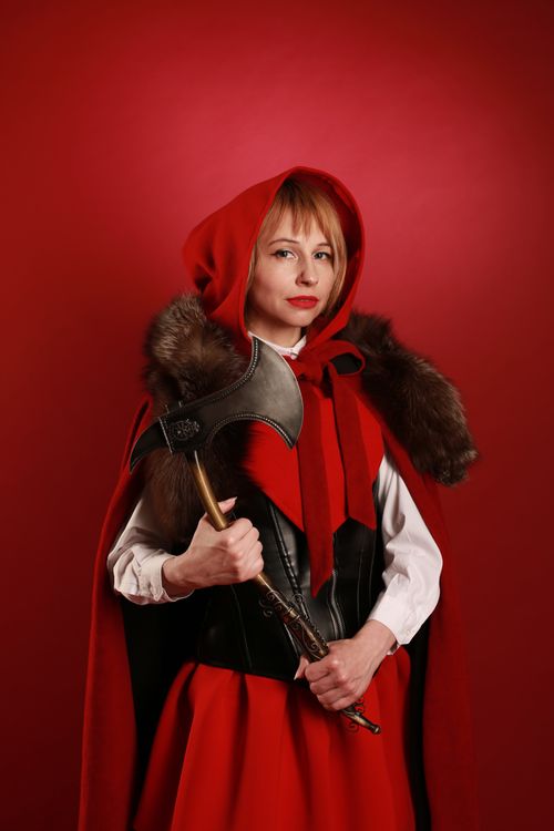 Free Woman in red hooded medieval costume holding a decorative axe in a studio setting. Stock Photo