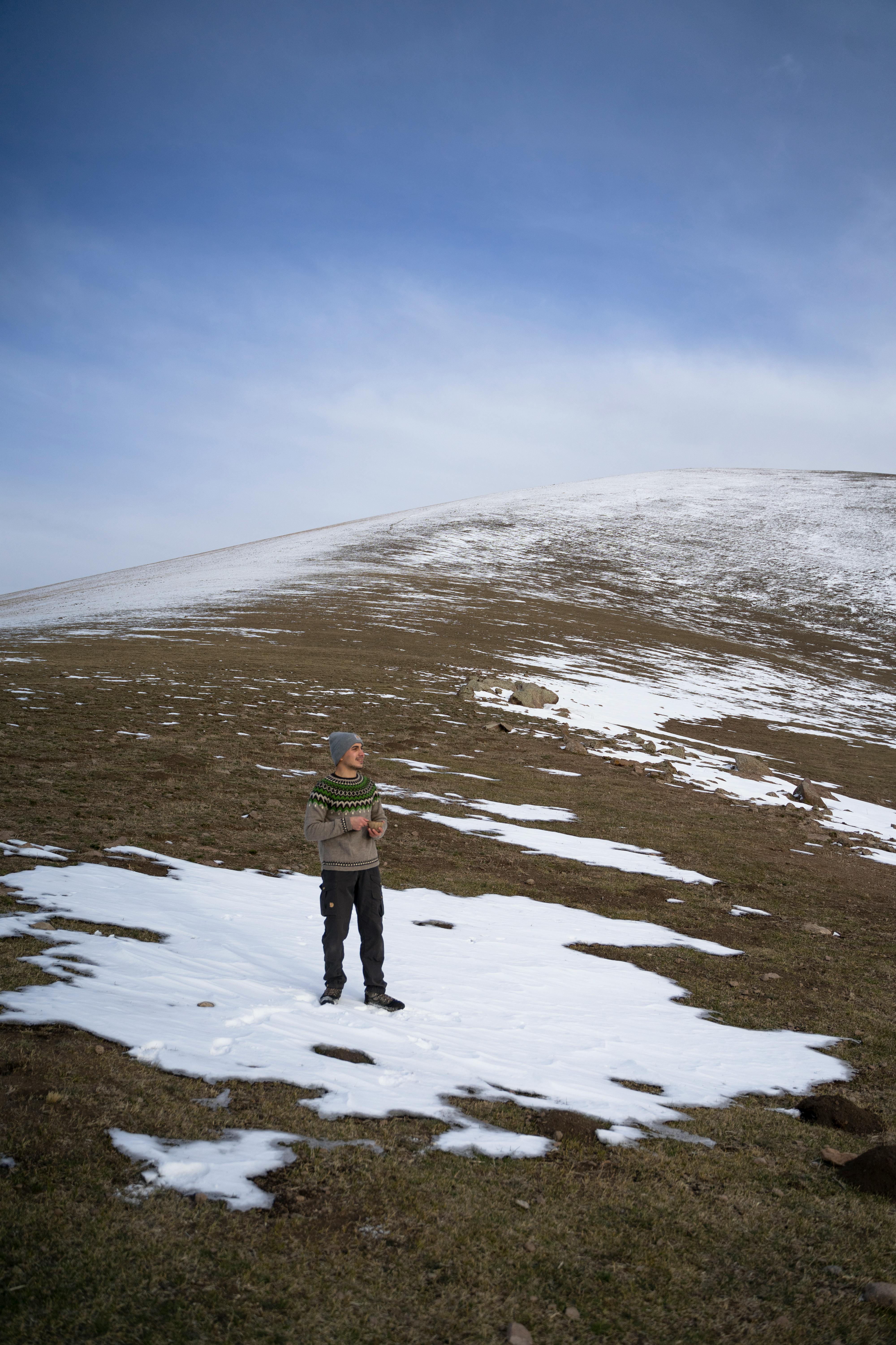 Prescription Goggle Inserts - A solitary person standing on a snowy hill, surrounded by brown grass and an expansive blue sky.