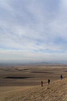 Hikers explore a vast, arid landscape under a cloudy sky, embodying adventure and solitude.