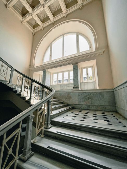 Pillars at arched window viewing stone stairway in old classic building with ornamental ceiling