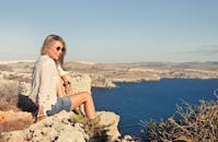 一名女子在马耳他姆加尔的悬崖上，沐浴着明媚的阳光，欣赏着壮丽的海景