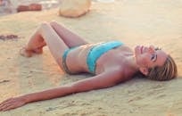 一名女子身穿蓝色泳衣，躺在马耳他沙滩上，享受着阳光明媚的夏日