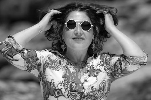 A fashionable woman smiling and holding her hair in a stylish outfit and sunglasses.