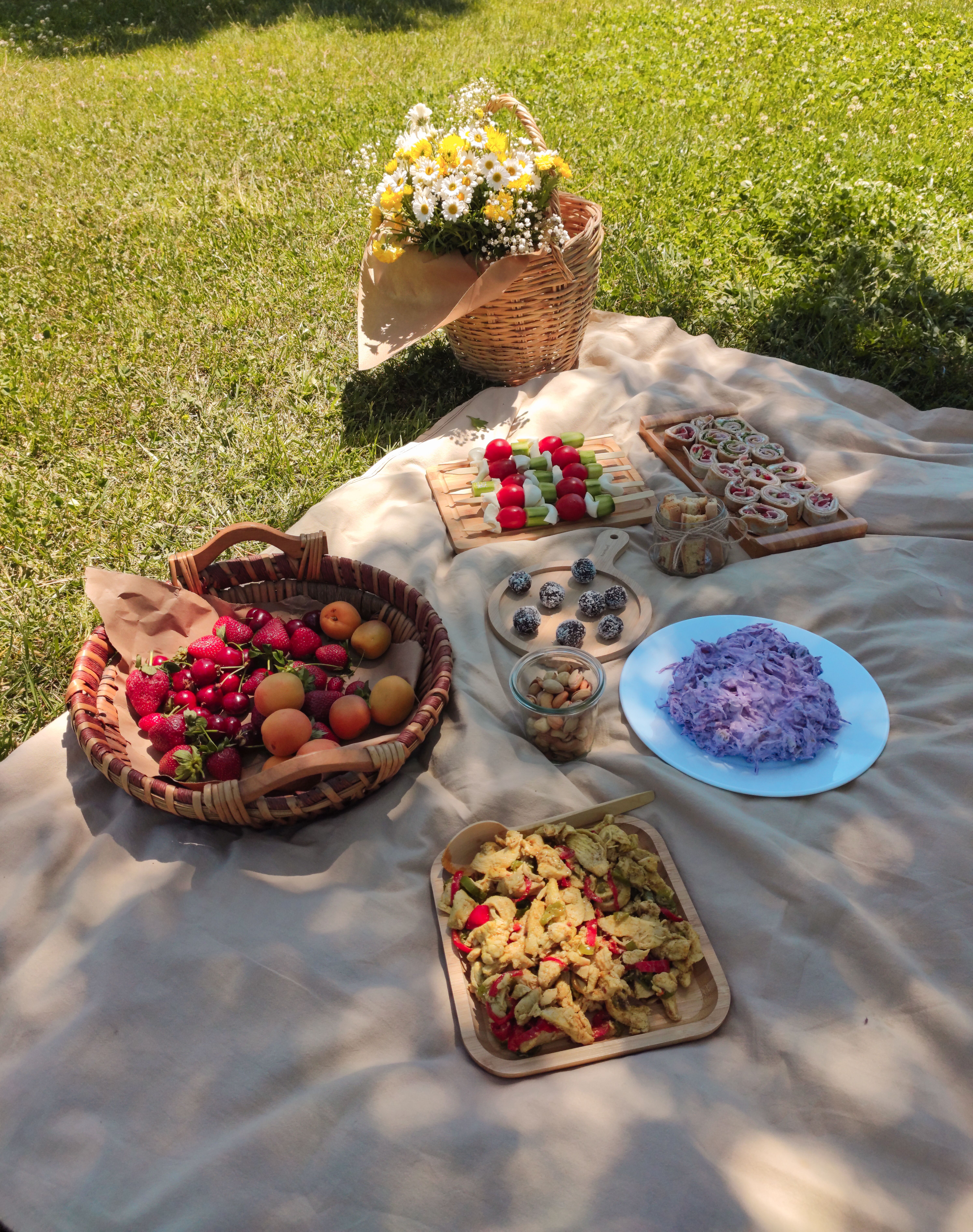 A vibrant outdoor picnic setup with fruits, pastries, and flowers on a sunny day.