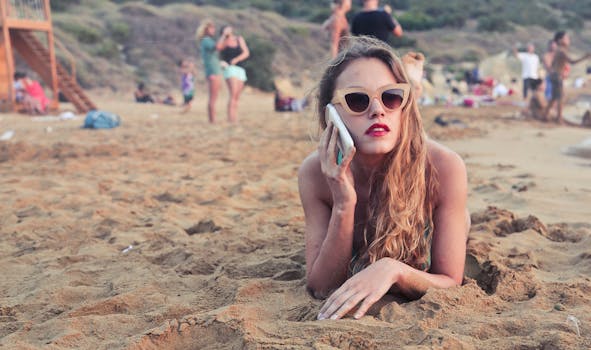 A woman with sunglasses relaxes on Mgarr Beach in Malta, talking on her smartphone.