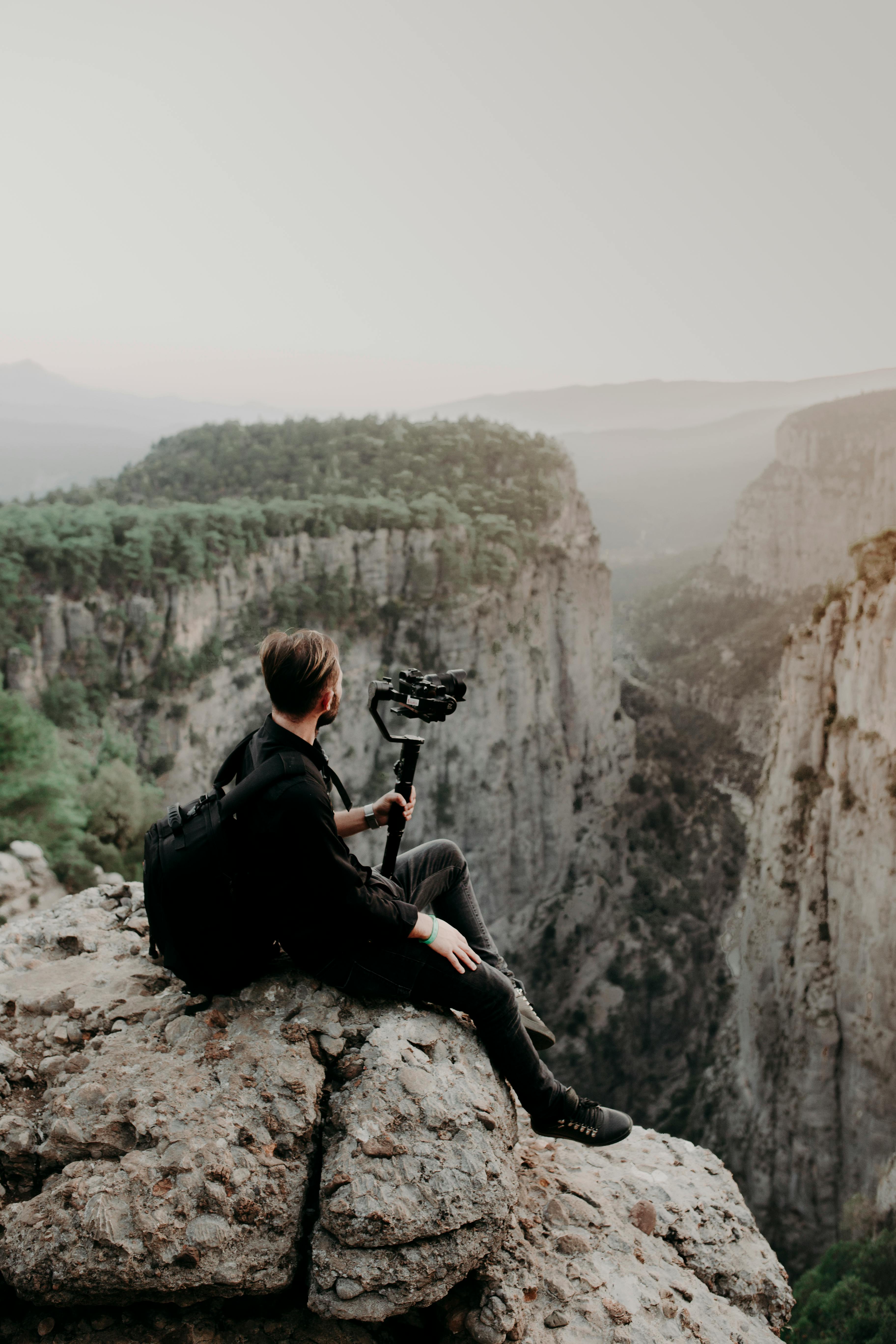 man sitting on edge of cliff with camera