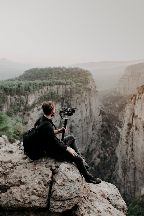 Free Man sitting on edge of cliff with camera Stock Photo