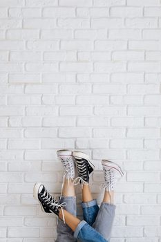 Casual legs wearing converse sneakers lean upside down on a white brick wall.